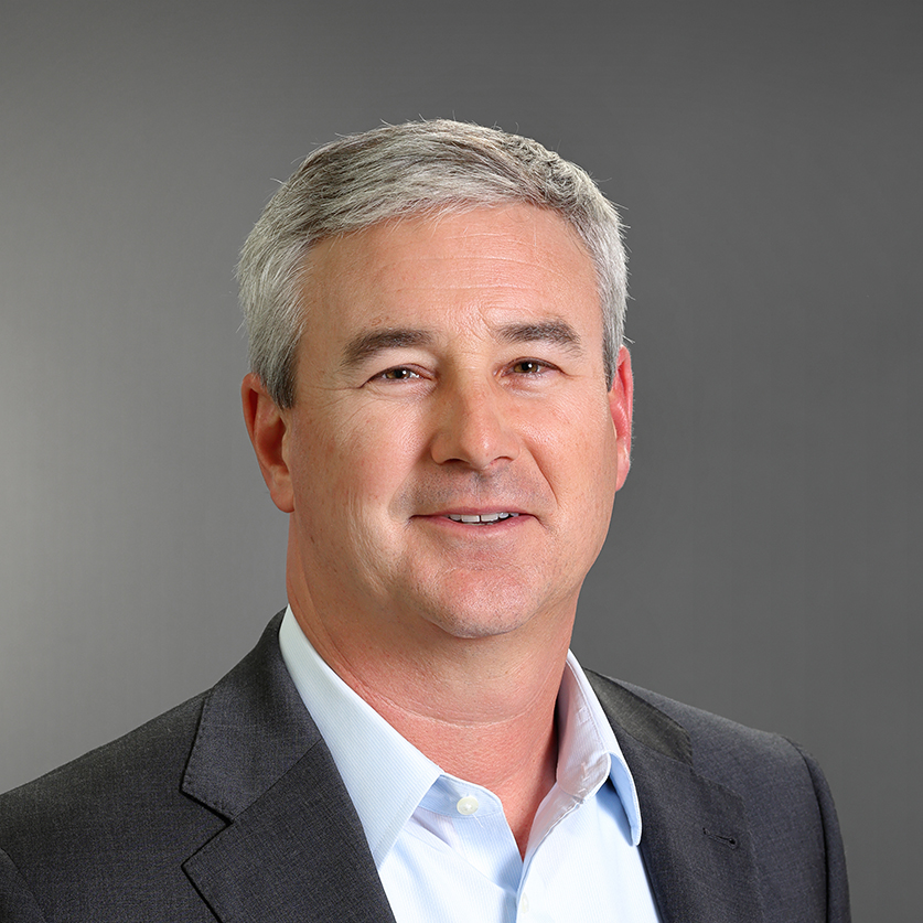 Professional headshot of Hunter Gibson smiling, wearing a dark gray suit jacket and light blue dress shirt against a gray background.