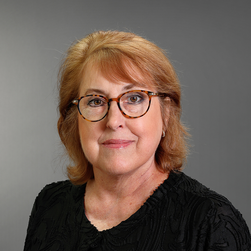 Professional headshot of Judy Wilson wearing tortoiseshell glasses and a black textured top against a gray background.