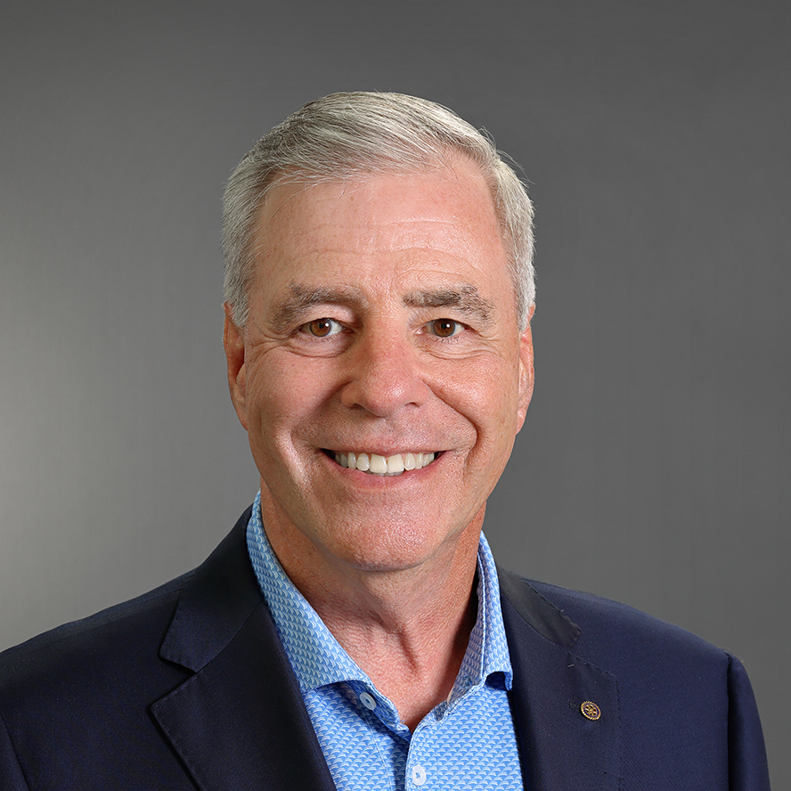 Professional headshot of Mike Snively smiling, wearing a navy blazer and blue patterned dress shirt against a gray background.