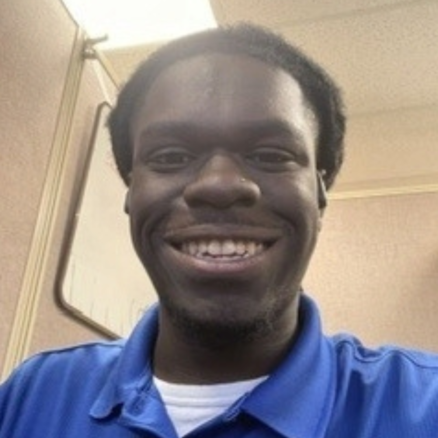 Jarvis smiles warmly at the camera, wearing a blue collared polo shirt over a white T-shirt. He is pictured indoors against a light-colored background